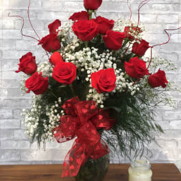 Red roses arranged in a glass vase with baby's breath and a red ribbon
