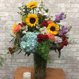 Mixed bouquet with sunflowers, roses, hydrangea, and lilies in a glass vase