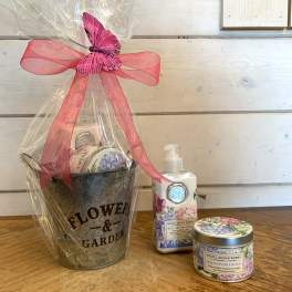 Gift basket with a flower garden bucket, lotion, and candle tied with a pink ribbon