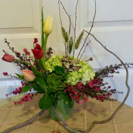 Mixed tulips and hydrangeas in a glass vase with curly branches