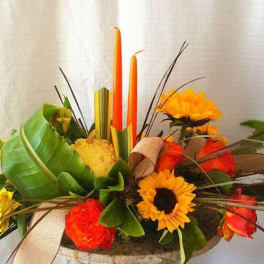 Orange and yellow floral arrangement with candles in a low container