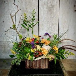 Mixed floral arrangement with yellow, purple, and orange blooms in a rustic container