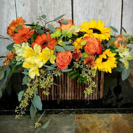Mixed bouquet of sunflowers, orange roses, and yellow flowers in a rustic container