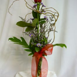 Tall red rose arrangement with purple filler flowers in a clear vase