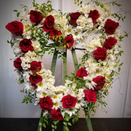 Heart-shaped floral wreath with red roses and white daisies on a stand