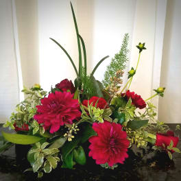 Low floral arrangement with magenta blooms and red roses in a dark container