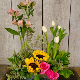 Mixed bouquet with sunflowers, pink roses, white tulips, and pink alstroemeria in a metal container