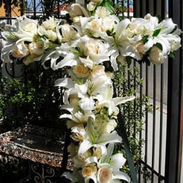 White lilies and cream roses arranged on a tall cross display