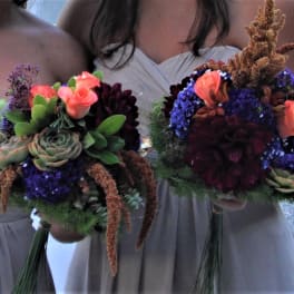 Two bridesmaids hold bouquets with succulents, coral roses, and dark blooms.