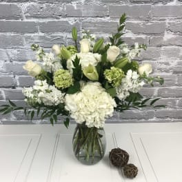 White roses, hydrangeas, lilies, and green blooms in a glass vase