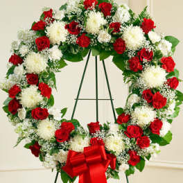 Standing wreath of red roses and white flowers with a large red bow