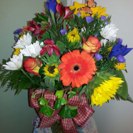 Mixed bouquet with gerbera daisies, roses, and a butterfly decoration in a vase