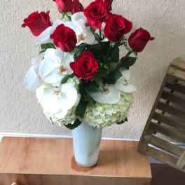 Red roses and white orchids arranged in a tall white vase