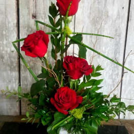 Red roses arranged in a white vase with green foliage