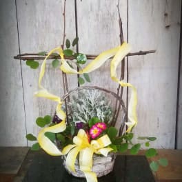 Basket arrangement with pink flowers, greenery, and yellow ribbon on a twig frame