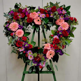 Heart-shaped floral wreath with roses, gerbera daisies, and purple blooms on an easel