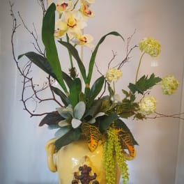Tall floral arrangement with yellow orchids in a decorative ceramic vase