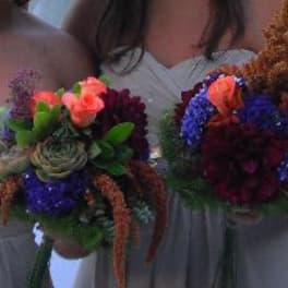 Two bridesmaids hold colorful bouquets with succulents and orange blooms.