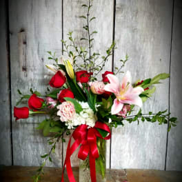 Bouquet of red roses and pink lilies in a glass vase with a red ribbon
