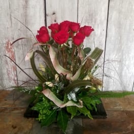 Tall arrangement of red roses with decorative ribbon and foliage