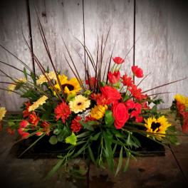 Low floral arrangement with red, yellow, and orange blooms in a black container