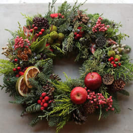 Holiday wreath with evergreen branches, red berries, apples, and pinecones