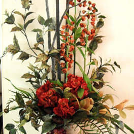Tall floral arrangement with red blooms and orange spray flowers in a vase