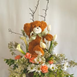 Teddy bear in a flower basket with tulips, roses, and daisies
