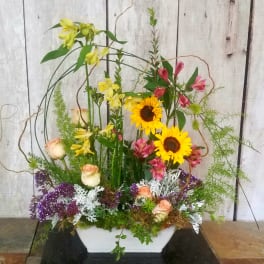 Tall mixed floral arrangement in a white rectangular vase with sunflowers and roses