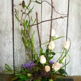 Tall floral arrangement with white roses and purple accents in a pink vase