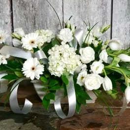 White floral arrangement with daisies, roses, and ribbon in a low container