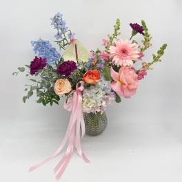Mixed pastel flower arrangement in a glass vase with a pink ribbon
