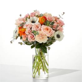 Bouquet of blush roses, white anemones, and orange ranunculus in a clear glass vase