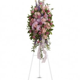 Standing floral spray with pink roses and purple flowers on a white easel