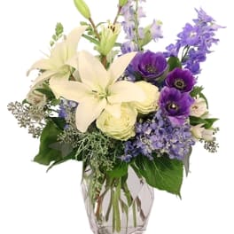 Bouquet of white lilies and purple flowers in a clear glass vase