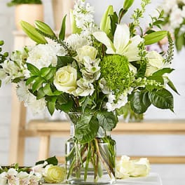 White floral arrangement in a clear glass vase with lilies and roses