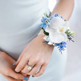 Wrist corsage with white orchid and blue flowers on a pearl bracelet worn with a light blue dress
