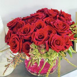 Red roses arranged in a clear glass vase with small green filler flowers
