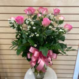 Pink roses arranged in a clear glass vase with a pink ribbon bow