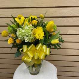 Yellow floral bouquet in a glass vase with a large yellow ribbon