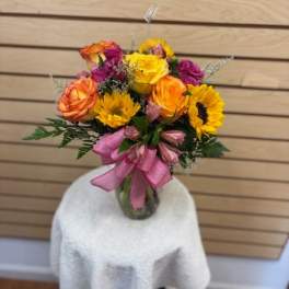 Bouquet of yellow, orange, and pink flowers in a glass vase with a pink ribbon