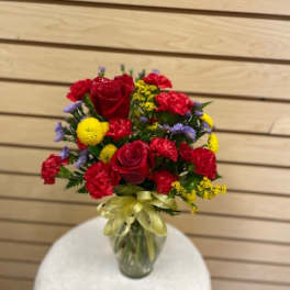 Bouquet of red roses, carnations, and yellow and purple filler flowers in a glass vase