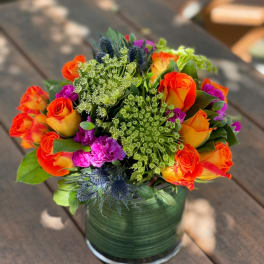 Bright mixed bouquet of orange roses and purple flowers in a glass vase