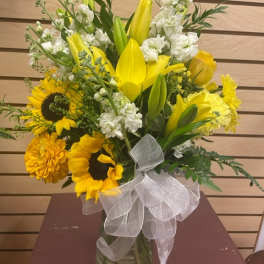 Yellow lilies and sunflowers in a glass vase with a white ribbon