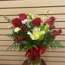 Red roses and white lilies in a glass vase with a red ribbon