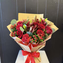 Bouquet of red roses and lilies wrapped in tan paper with a red ribbon