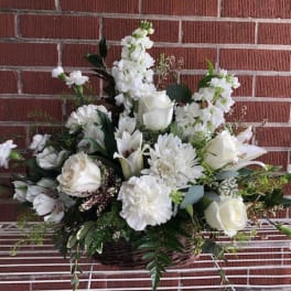 White floral arrangement in a wicker basket with roses and lilies