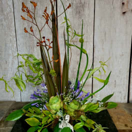 Tall tropical arrangement with green succulents and purple flowers on a black base