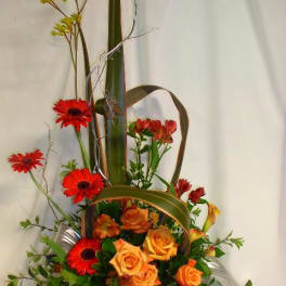 Tall floral arrangement with orange roses and red gerbera daisies in a black vase