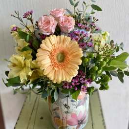 Mixed bouquet with pink roses and a peach gerbera daisy in a floral tin